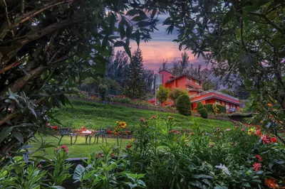 a garden with flowers and a red house in the background at Willow Hill by Nature Resorts and Stays in Ooty