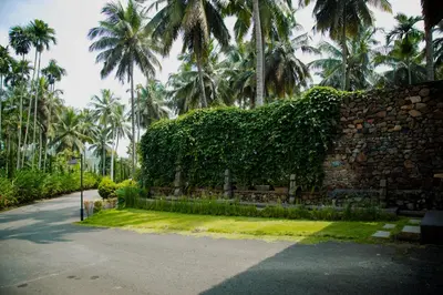 a stone wall with palm trees in the background at Maayaa riverside villa by KPM Tripenta in Attappādi