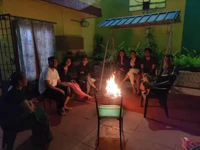 a group of people sitting around a fire in a room at Shanthi Villa in Coonoor
