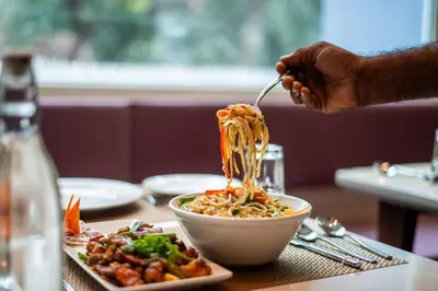 a person eating noodles from a bowl on a table at Lilac Hotel Guruvayur in Guruvāyūr