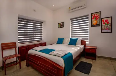 a bedroom with a bed and a chair and two windows at The Vogue - Luxury Private Pool Villa , Athirappilly in Athirappilly