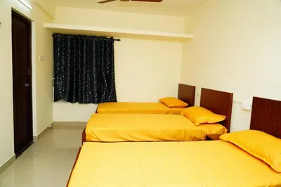 two beds in a room with yellow sheets and a window at Meadow Comfort Stay in Coimbatore
