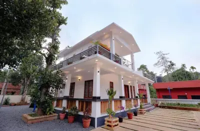 a white house with potted plants in front of it at Greenfield Homestay in Vythiri