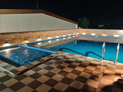 a swimming pool with lights on a house at night at Hotel Newline Orchid in Guruvāyūr