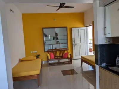 a living room with yellow walls and a kitchen with a couch at Athreyas@60/A in Mysore