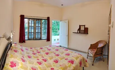 a bedroom with a bed and a chair and a window at Raintree Garden in Mysore