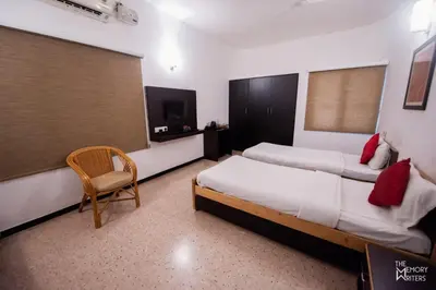 a hotel room with two beds and a chair at Corner Stay Serviced Apartment-Racecourse in Coimbatore