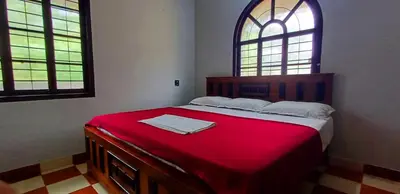 a bedroom with a bed with a red blanket and two windows at Kalpetta Peace Villa in Kalpetta