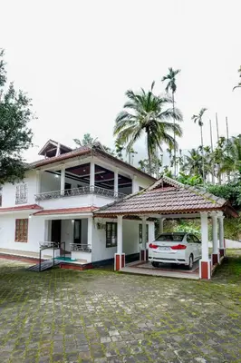 a white house with a car parked in front of it at Wayanad Palm Grove Retreat G Floor in Sultan Bathery