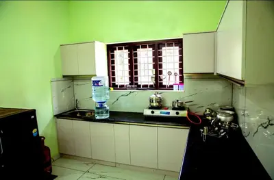 a kitchen with green walls and white cabinets and a window at DREAMS VILLA Near Rajagiri Hospital in Alwaye