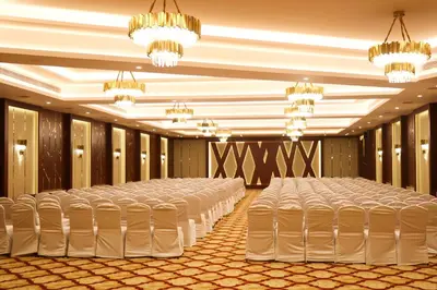 a banquet hall with rows of white chairs and chandeliers at Jenneys Residency in Coimbatore