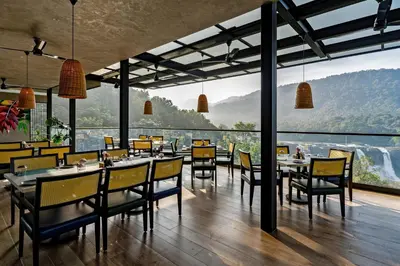 a restaurant with tables and chairs and a large window at Flora Misty Falls Athirappilly in Athirappilly