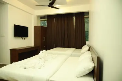 a bedroom with two beds with white sheets and a television at AROMA INN in Kalpetta