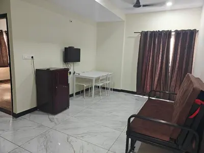 a room with a tv and a chair and a table at Comfort Cove Apartments in Mysore