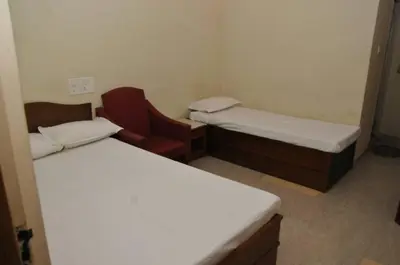a small room with two beds and a red chair at MYSORE MAHALAKSHMI ROOMS in Mysore