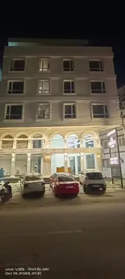 a large white building with cars parked in front of it at Hotel Emora Tree in Mysore