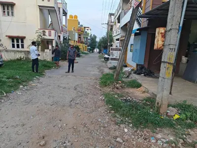 two men standing on a dirt road next to buildings at 2Bhk holiday home in Mysore