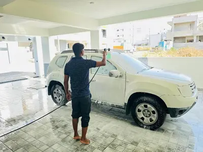 a man washing a white truck with a hose at Oryx Hotel Apartments in Mysore