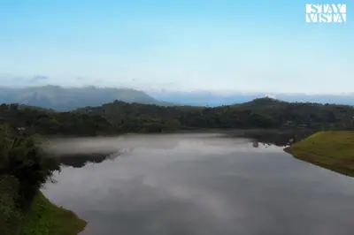 a misty lake in the middle of a valley at Rivera The Lake View with Indoor Games by StayVista in Wayanad