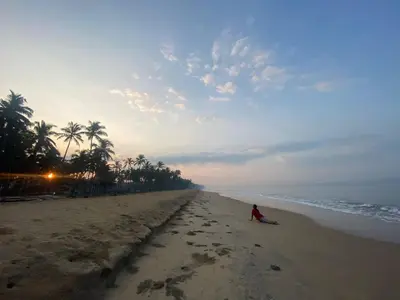 a person sitting on the beach near the ocean at Casa Ganesha beach villa in Irimbranallūr
