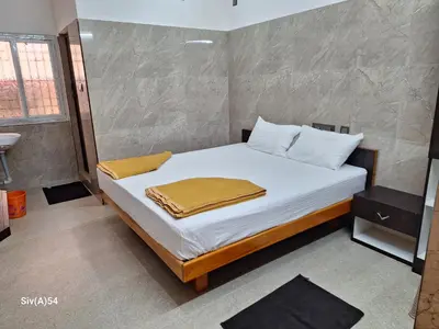 a bedroom with a bed with white sheets and a sink at Viruksham Residency in Palani