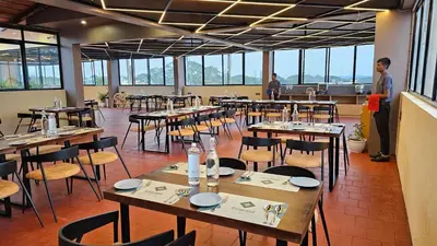 a restaurant with tables and chairs with people standing in the background at Emerald Urban Comforts in Mysore