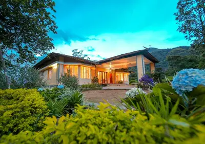 a house with the lights on in a garden at Viriparai Tea Bungalow Munnar by VOYE HOMES - Surrounded by Tea Plantations in Munnar