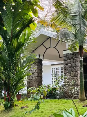 a house with a stone wall and palm trees at The Mallika Holidays in Mananthavady