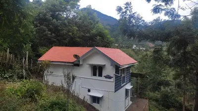 a white house with a red roof on a hill at jacaranda resorts in Kanthalloor