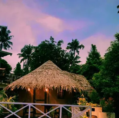 a hut with a straw roof with palm trees at Village of Blossom in Ernakulam