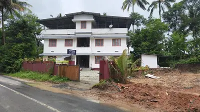 a white house with a black roof on the side of the road at Souparnika Lakeview Homestay LLP in Wayanad