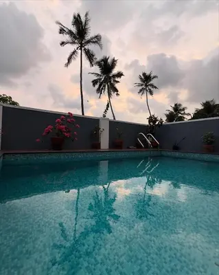 a swimming pool with palm trees in the background at Kappad Beach House by Kisah Stays in Kappad
