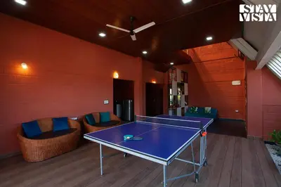 a ping pong table in a room with blue chairs at Golden Triangle by VEO - Part of StayVista in Hampāpura