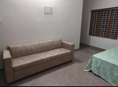 a brown couch sitting in a room with a bed at Homestay Guruvayur, 2 AC Bedrooms, Hall, Veranda, Kitchen in Guruvāyūr