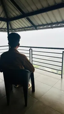 a man sitting in a chair looking out the window at Western Ghats Holiday Home in Kalpetta