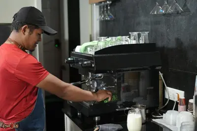 a man is making a drink in a kitchen at Hotel Bluebell in Kozhikode