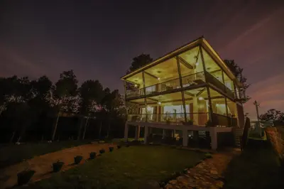 a house with large glass windows at night at Tranquil Haven Kotagiri in Kotagiri