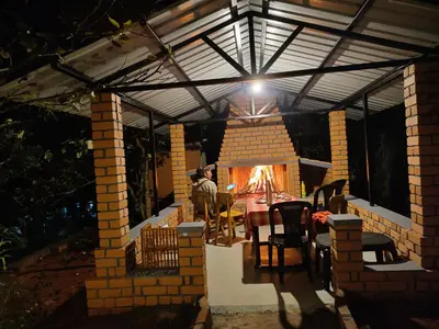 a man sitting at a table in a house with a fireplace at Silver Spruce Glass Villa 1BHK Kotagiri in Kotagiri
