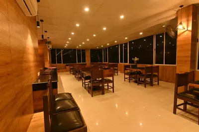 a restaurant with wooden tables and chairs and windows at THE DAWN HOTEL in Mysore