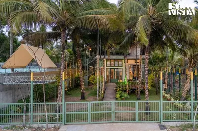 a house with palm trees in front of a fence at StayVista at Own The Beach Life - 1 BHK Pet Friendly - Beach View in Trichūr