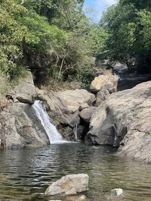 a waterfall on the side of a river with rocks at Wetlands Wayanad Pool Resort with Natural Waterfalls in Padinjarathara