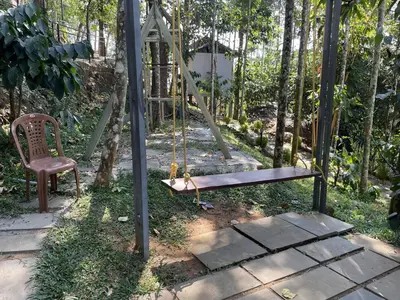 a swing and a chair in a garden at Wetlands Wayanad Pool Resort with Natural Waterfalls in Padinjarathara