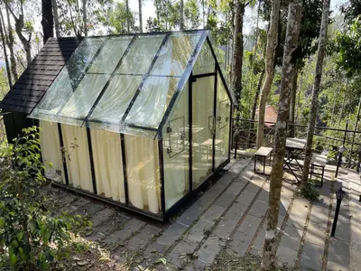 a glass house with a bench on a deck at Wetlands Wayanad Pool Resort with Natural Waterfalls in Padinjarathara