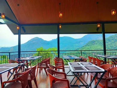 a restaurant with tables and chairs with mountains in the background at Nexstay Karimb Resorts in Vallikavungal