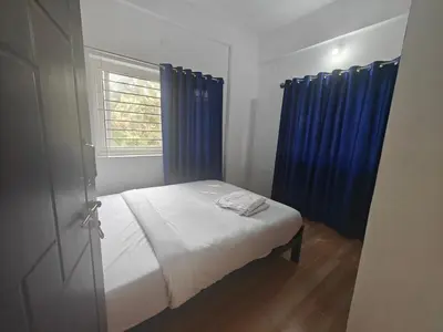 a bedroom with a bed with blue curtains and a window at Urban Nest Residence in Mysore