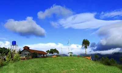 a house on top of a grassy hill with a cloudy sky at Vrindhavan Mist City Resorts in Kanthalloor