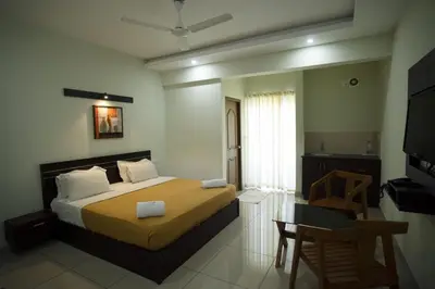 a bedroom with a bed and a table and a kitchen at AKAN HOTEL AND RESIDENCE in Wayanad