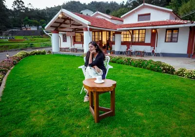 a woman sitting in a chair next to a table at Lauriston Ooty Town Heritage Bungalow by VOYE HOMES in Ooty