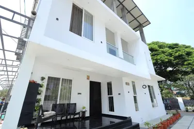 a white building with a black door and chairs at Eazy Homes in Palakkad