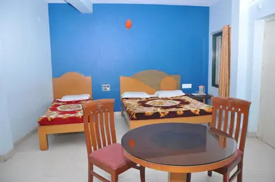 a room with two beds and a table and chairs at Vinayaka Deluxe Lodge in Kushālnagar
